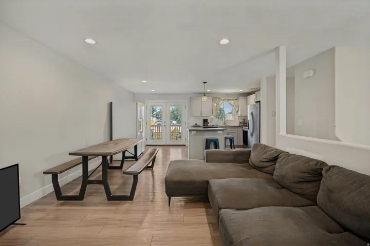 Recessed lighting, wood-finish flooring, white walls, double glass pane doors, and a kitchen bar with pendant lighting