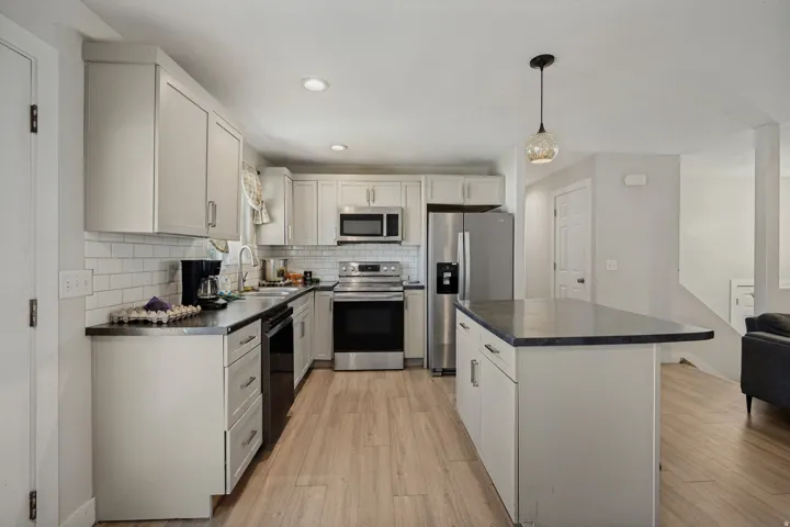 Kitchen featuring wood-finish flooring, white cabinetry, dark countertops, a subway tile backsplash, and stainless steel appliances