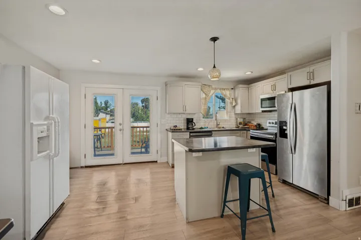 Kitchen featuring wood-finish flooring, recessed lighting, white cabinetry, a central island with a countertop, and a stainless steel refrigerator