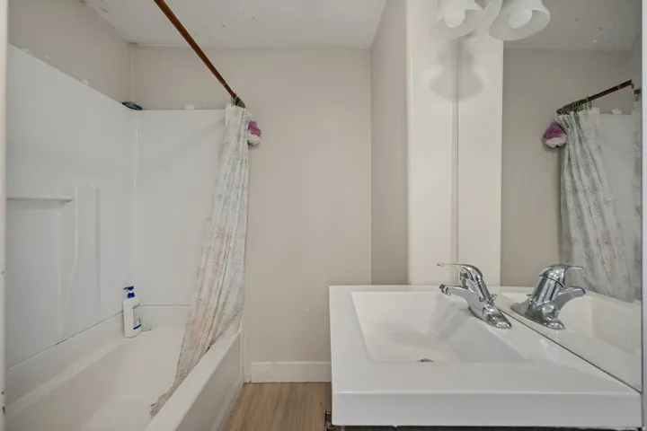 White vanity with integrated sink, chrome faucet, wall-mounted mirror, and overhead lighting