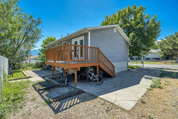 Raised wood deck with natural finish railings, exterior siding with a light gray finish, double French patio doors, and concrete slab foundation