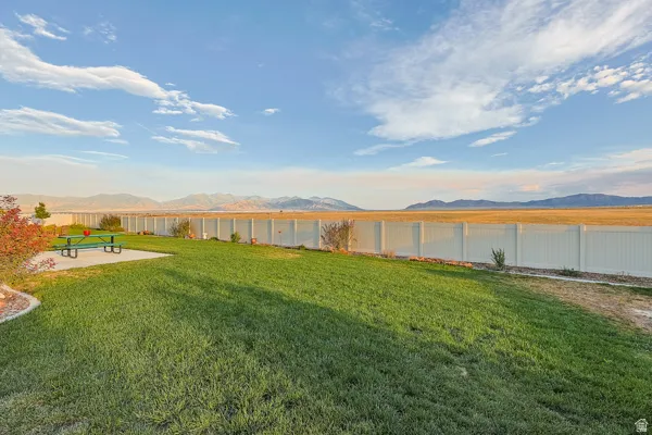 Expansive grass lawn with a concrete patio area, surrounded by a white privacy fence