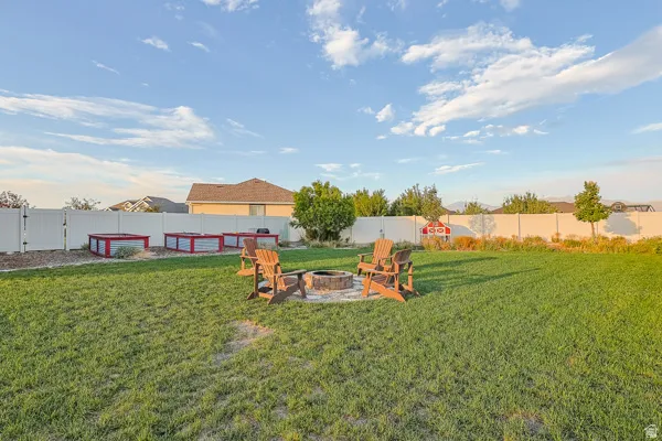 Expansive grassy backyard featuring a fire pit area, privacy fencing, and multiple raised garden beds