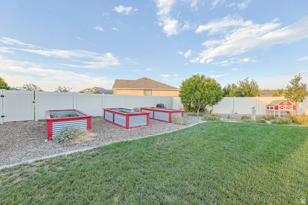Expansive backyard featuring a lush lawn, white privacy fencing, and multiple raised garden beds