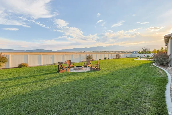 Expansive grassy yard with a fire pit area, concrete patio, perimeter fencing, and distant mountain scenery