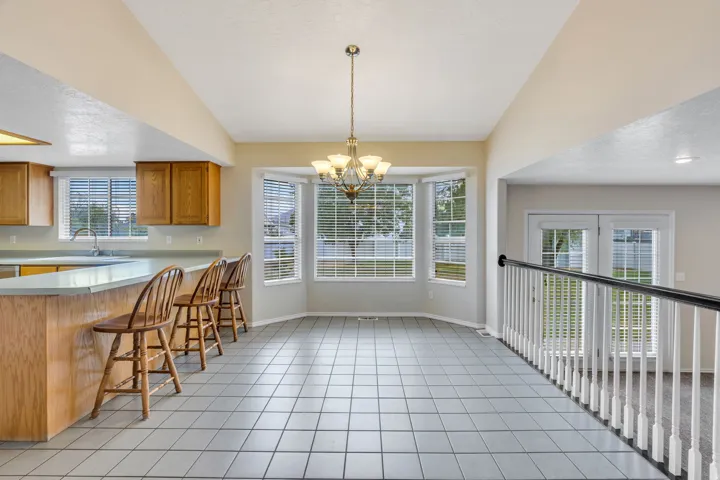 Kitchen bar seating with light wood cabinetry, white tile flooring, bay windows, and a multi-arm chandelier
