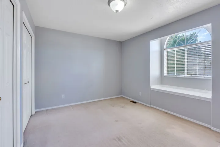 Bright secondary bedroom with expansive natural light from a large picture window, neutral wall finishes, neutral carpet flooring, and a spacious open floor plan ideal for multiple uses
