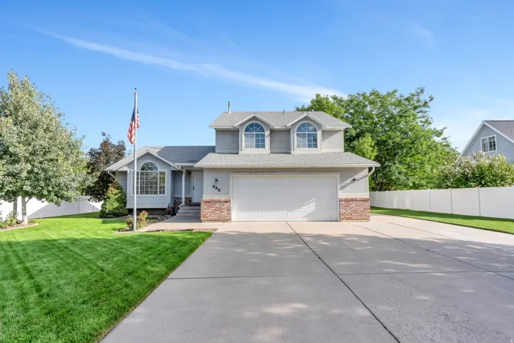 Stucco exterior with brick detailing, arched dormer windows, a two-car garage, and a concrete driveway