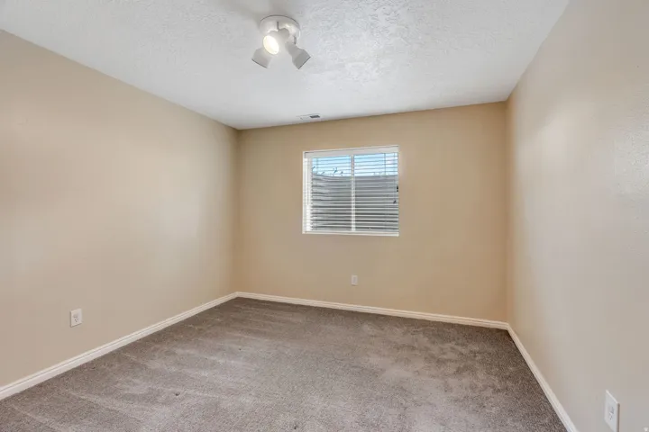 Neutral-toned walls, textured ceiling, window with blinds, and track lighting fixture
