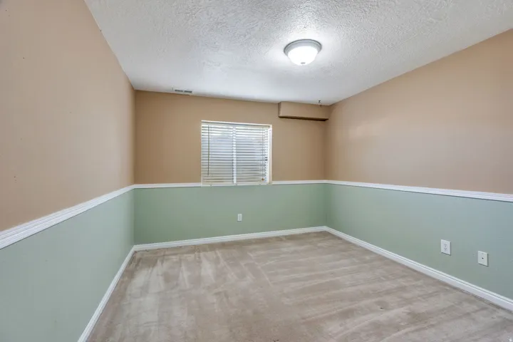 Wall-to-wall carpet flooring, two-tone painted walls, recessed window with horizontal blinds, and overhead flush-mount lighting