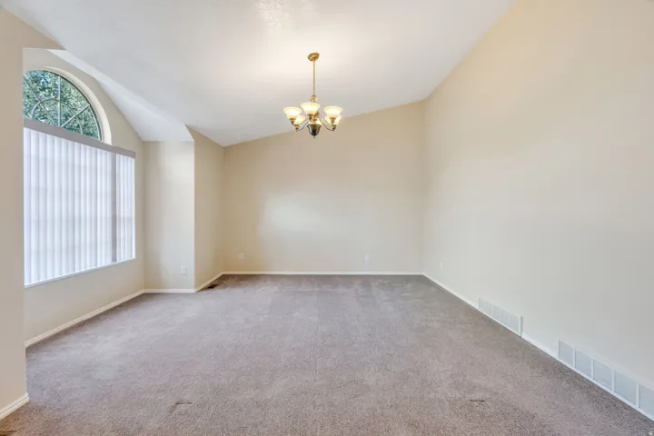 Vaulted ceiling, arched window, vertical blinds, and a brass chandelier