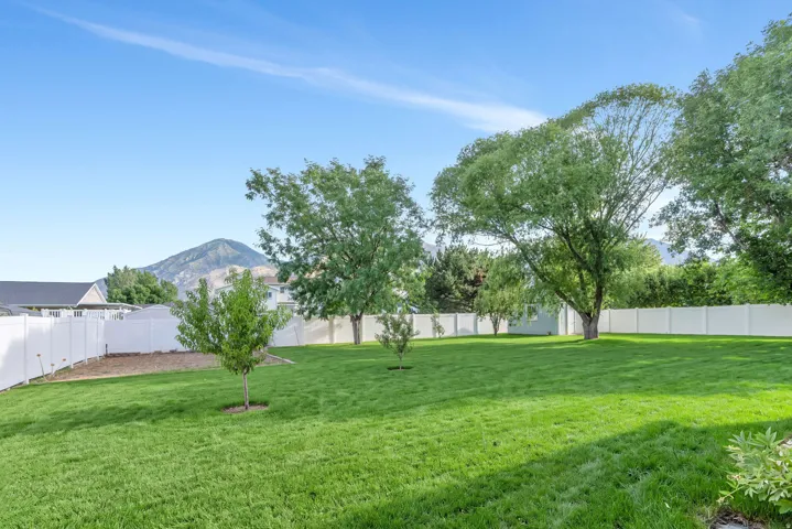 Spacious backyard with a manicured lawn, established trees, and a white privacy fence