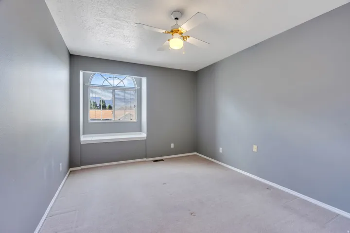 Arch-top window with integrated window seat, ceiling fan with light fixture, light gray carpeting, and textured walls