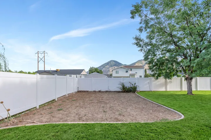 Expansive backyard with a manicured lawn, white privacy fencing, and mature trees