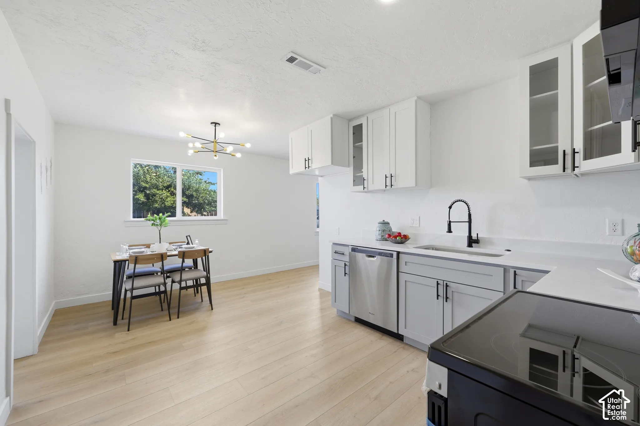 Wood-finish flooring throughout, white walls, double-pane window, modern lighting fixture, and white cabinetry with dark pulls