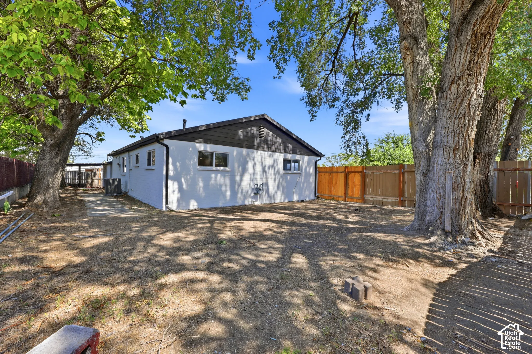 Enclosed backyard featuring mature trees, a wood privacy fence, and a white stucco exterior with dark trim