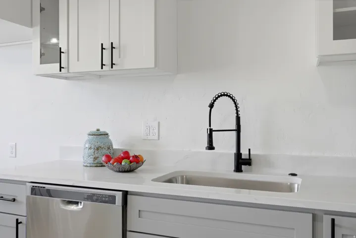 White upper cabinetry with black hardware, light gray lower cabinetry, stainless steel dishwasher, undermount stainless steel sink, and a black pull-down faucet