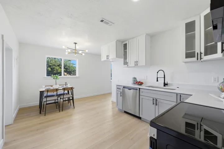 Wood-finish flooring throughout, white walls, double-pane window, modern lighting fixture, and white cabinetry with dark pulls