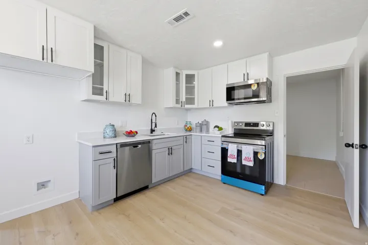 Modern kitchen featuring two-tone cabinetry, stainless steel appliances, a stainless steel sink with a matte black faucet, light-toned wood-finish flooring, and white countertops