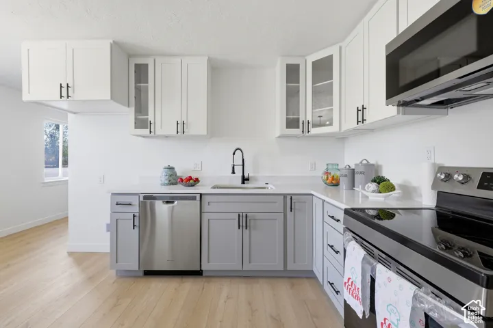 Two-tone cabinetry with glass-front uppers, stainless steel appliances, light-toned wood-finish flooring, and solid surface countertops