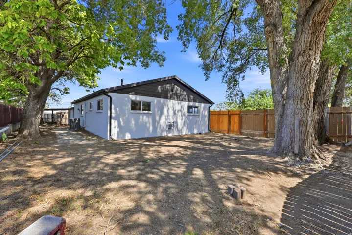 Enclosed backyard featuring mature trees, a wood privacy fence, and a white stucco exterior with dark trim