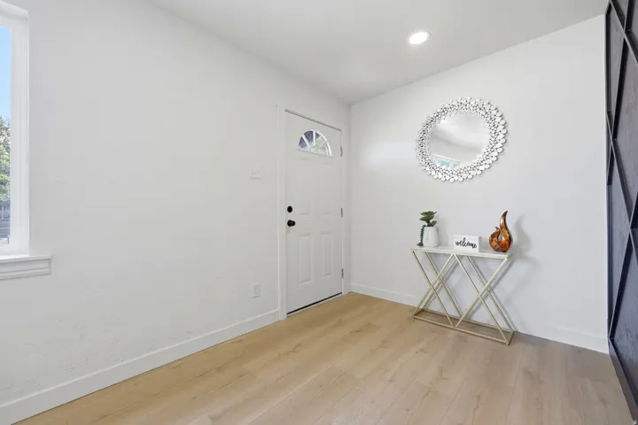 Light wood-finish flooring, white walls, recessed ceiling lighting, and a white entry door with a decorative window pane