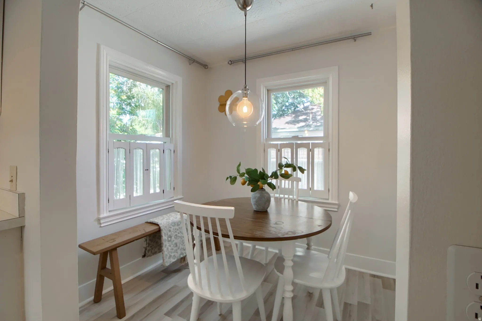 Light wood-finish flooring, white walls, two single-hung windows with white frames, and a clear glass pendant light fixture