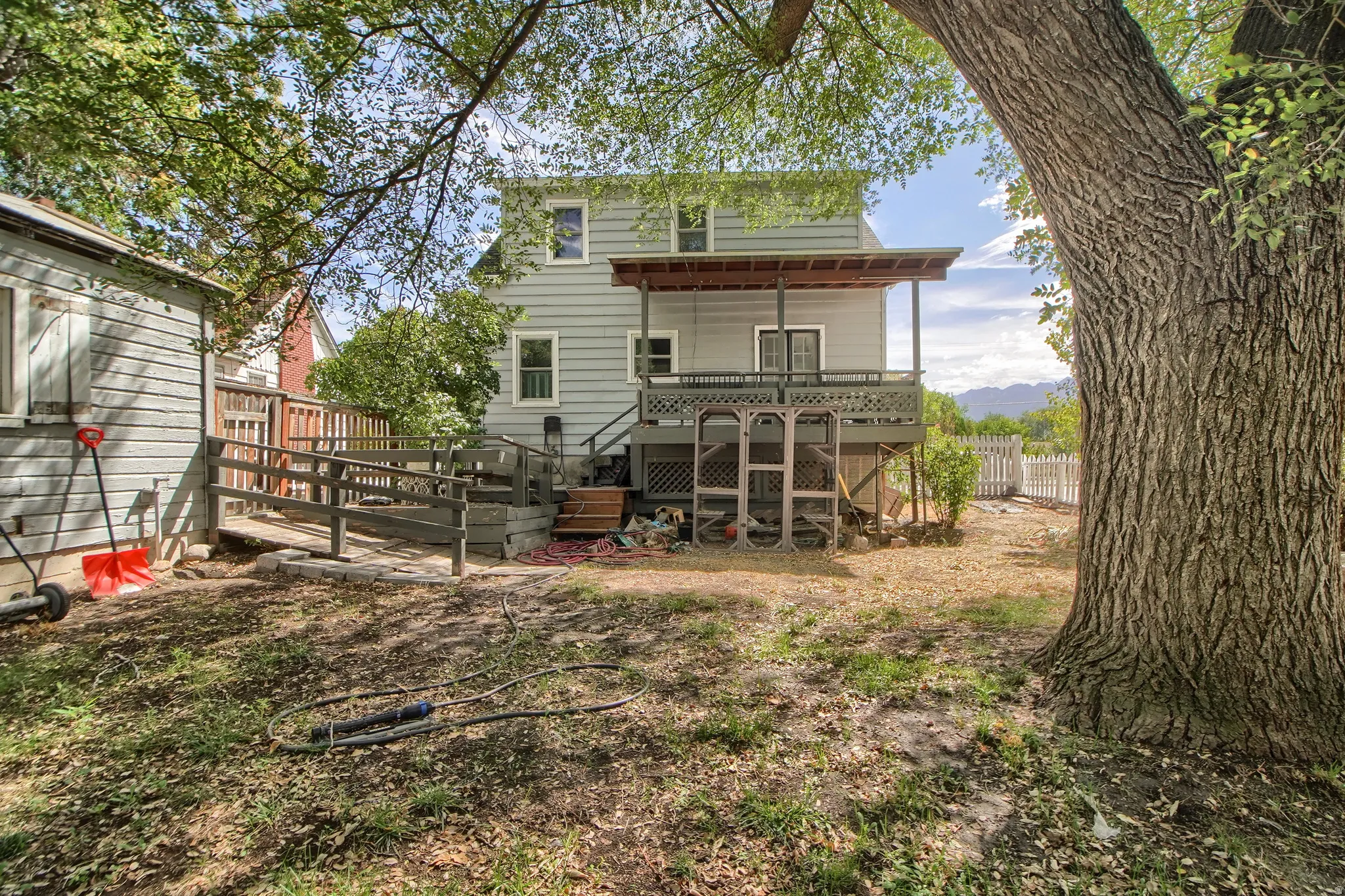 Rear exterior featuring a covered deck, lower-level patio, and a separate storage shed