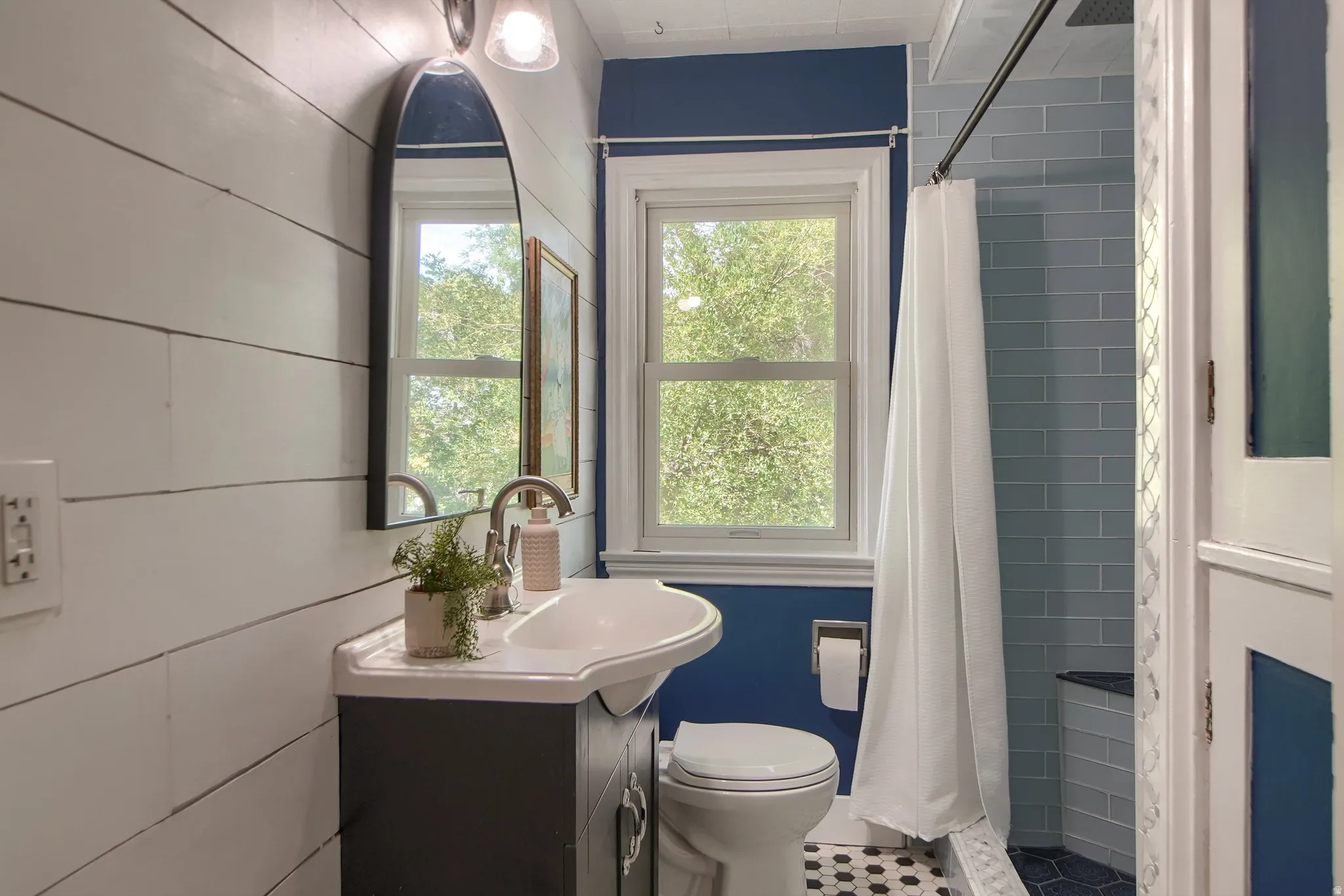 Bathroom featuring shiplap wall paneling, a pedestal sink with a vanity cabinet, a window, subway tile shower surround, and a hexagonal floor tile