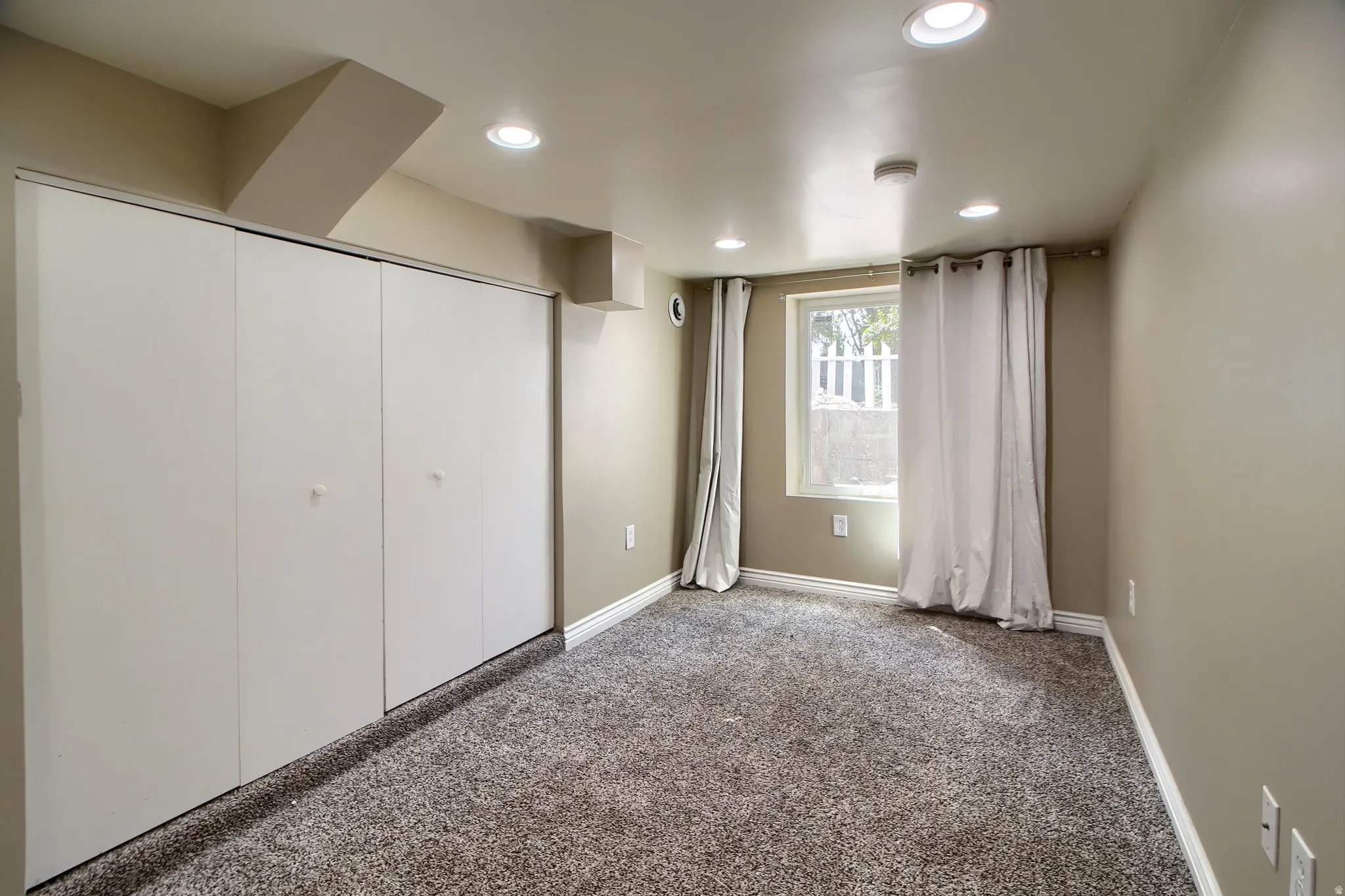 Wall-to-wall carpeting, recessed ceiling lighting, a window with white trim, and a full-height closet with sliding doors