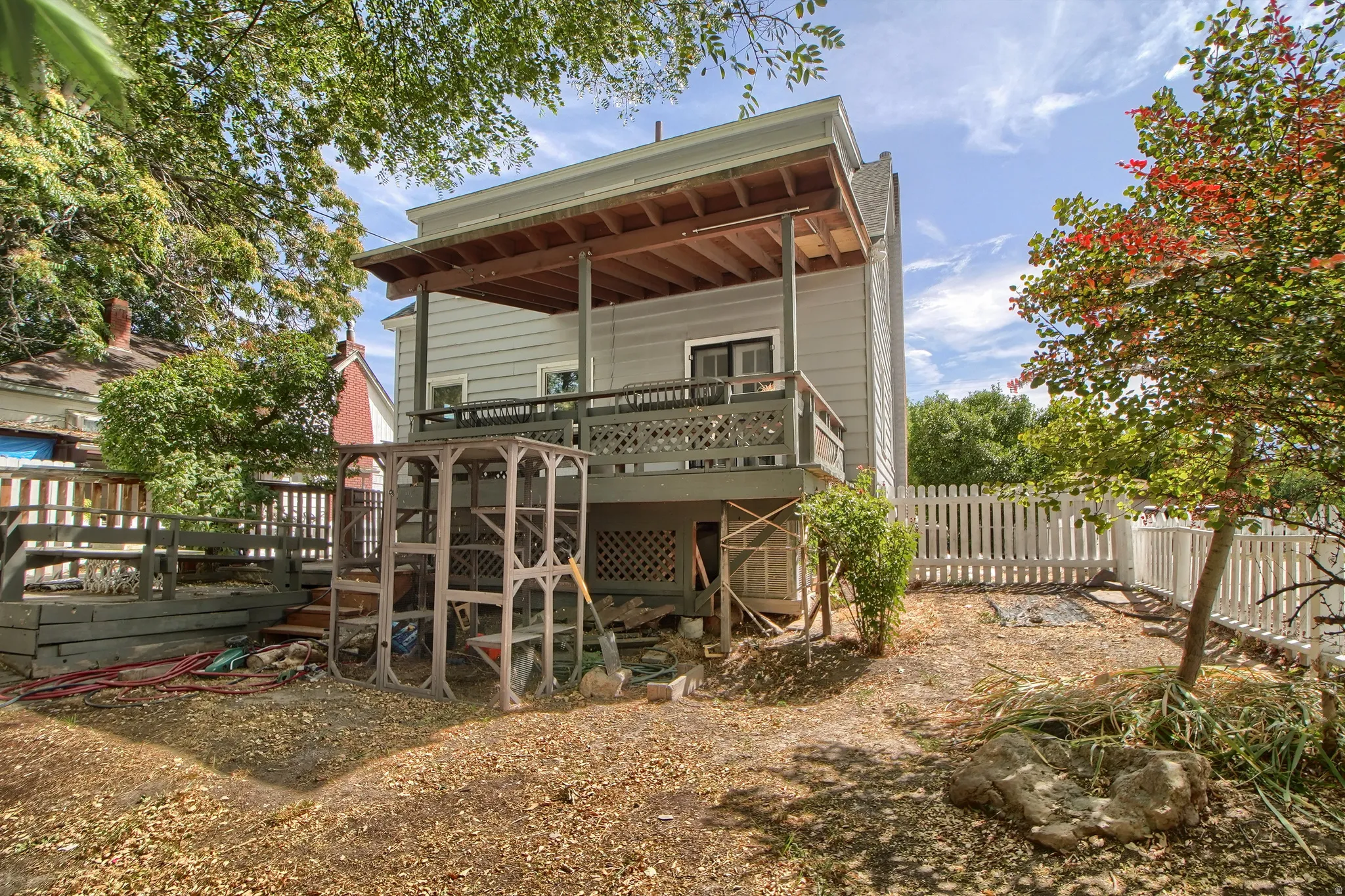 Rear exterior with an upper-level deck featuring a wood railing and lattice skirting, a lower-level retaining wall, and a white picket fence