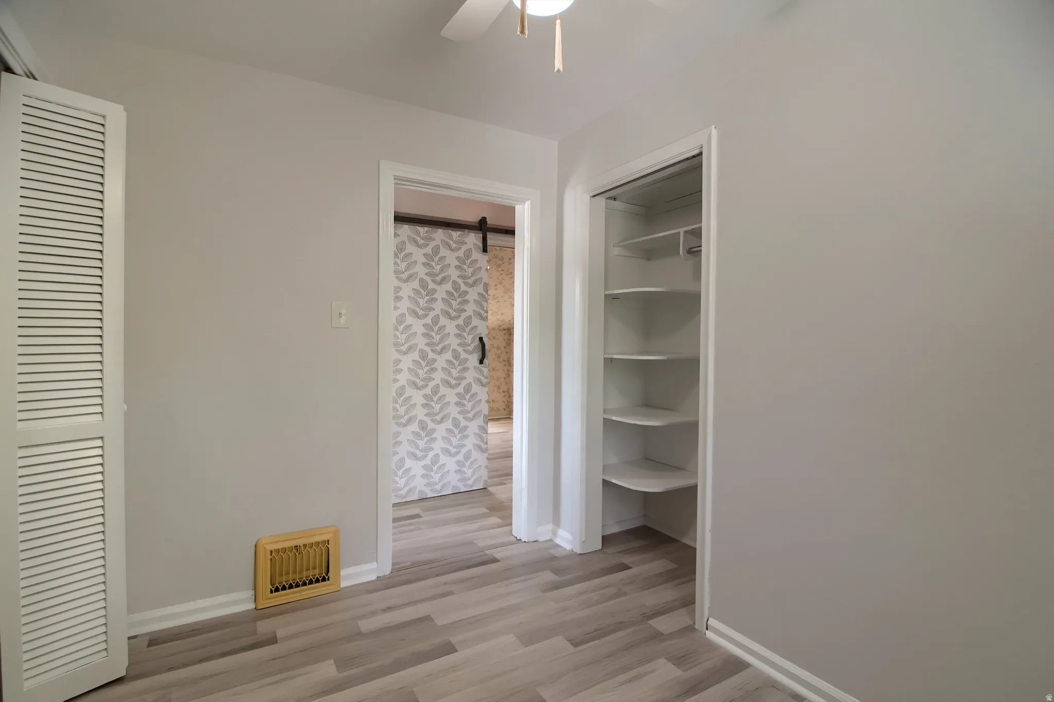 Wood-finish flooring, white trim, a built-in closet with shelving, a louvered bi-fold door, and a ceiling fan