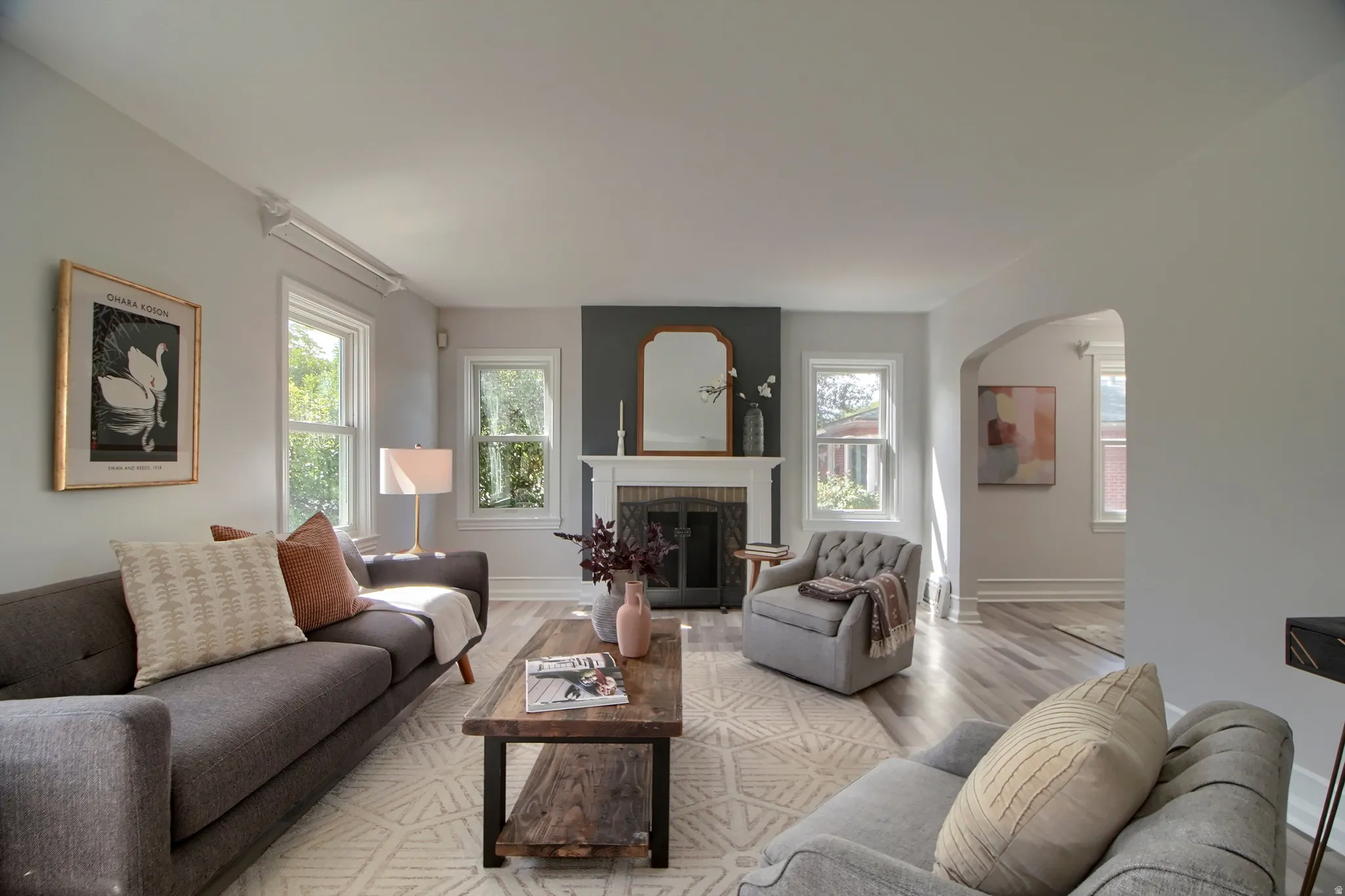 Living area featuring light wood-finish flooring, multiple windows, a decorative fireplace with a mantel, and an arched doorway