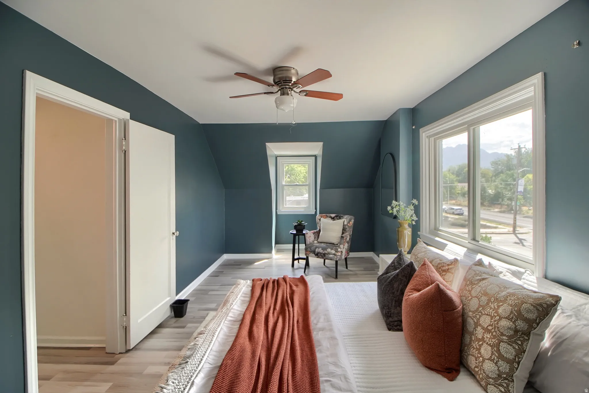 Wood-finish flooring, white trim, a ceiling fan, and multiple windows define this space