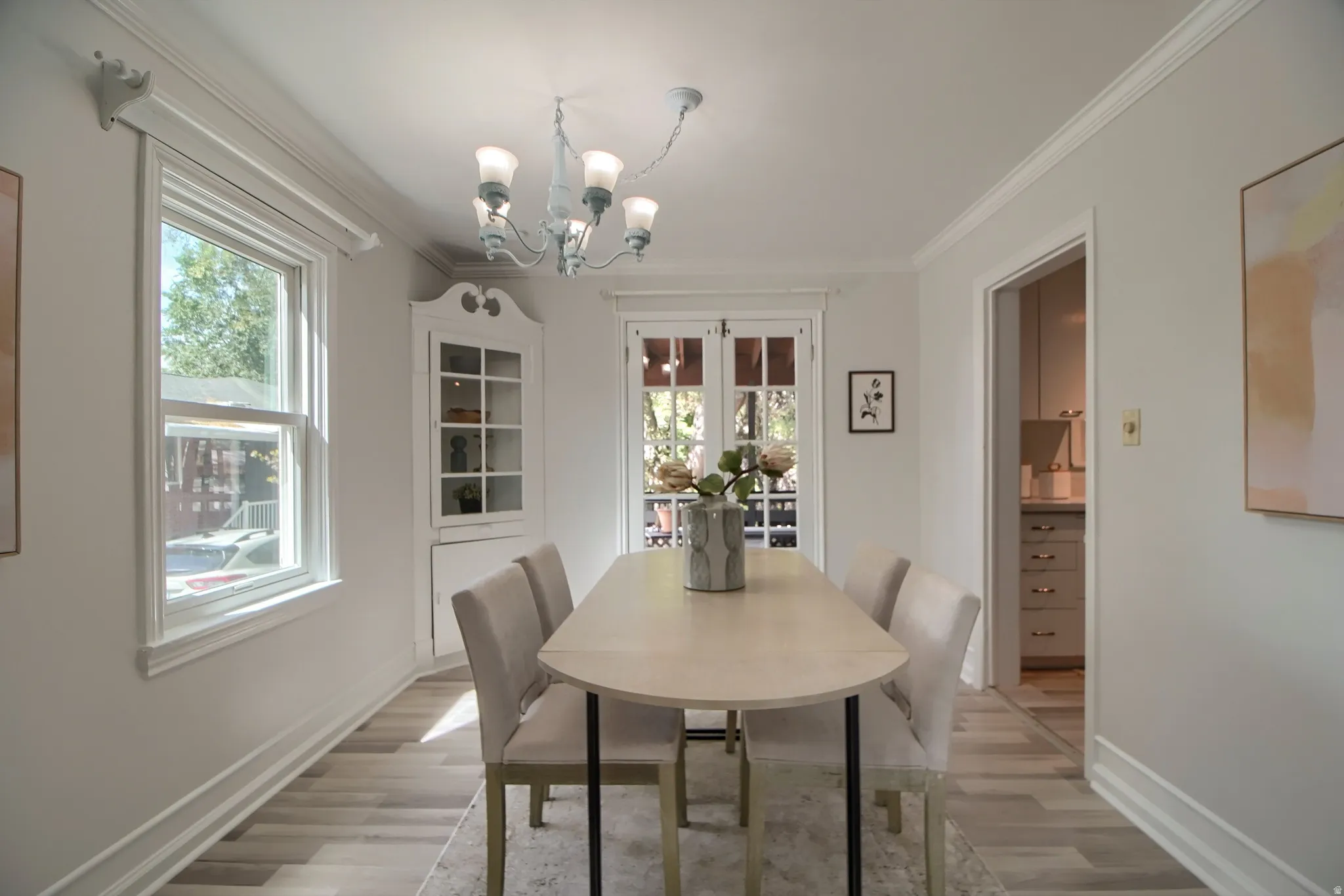 Wood-finish flooring, white crown molding, traditional chandelier, built-in corner cabinet with glass doors, and French doors with transoms