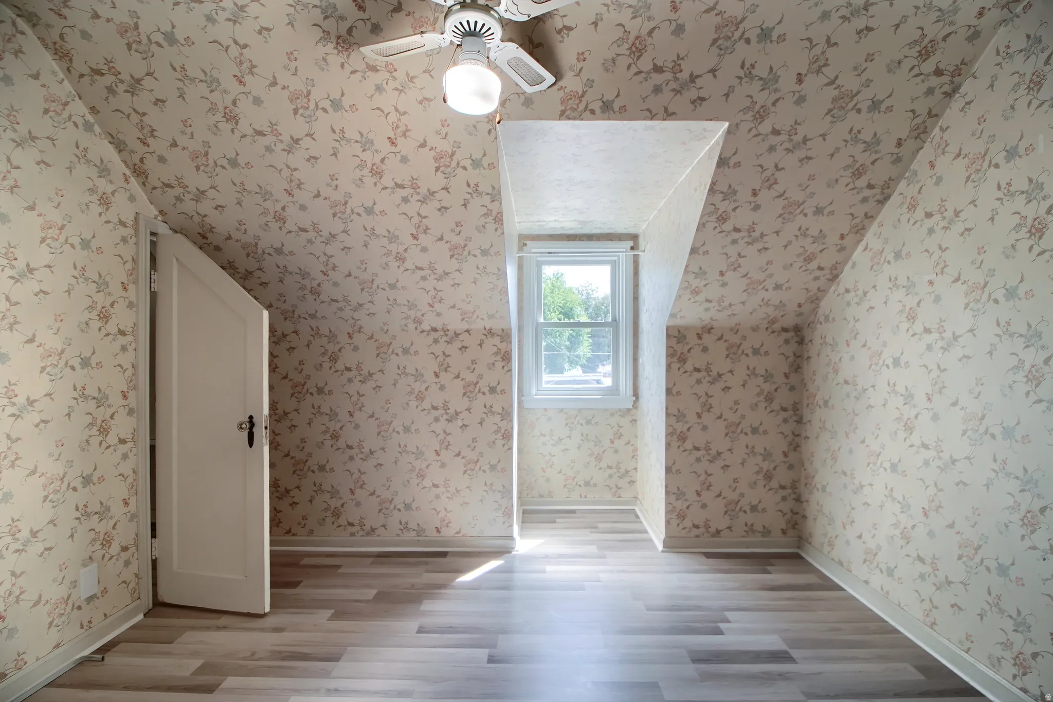 Room featuring sloped ceilings, a single-pane window, and wood-finish flooring