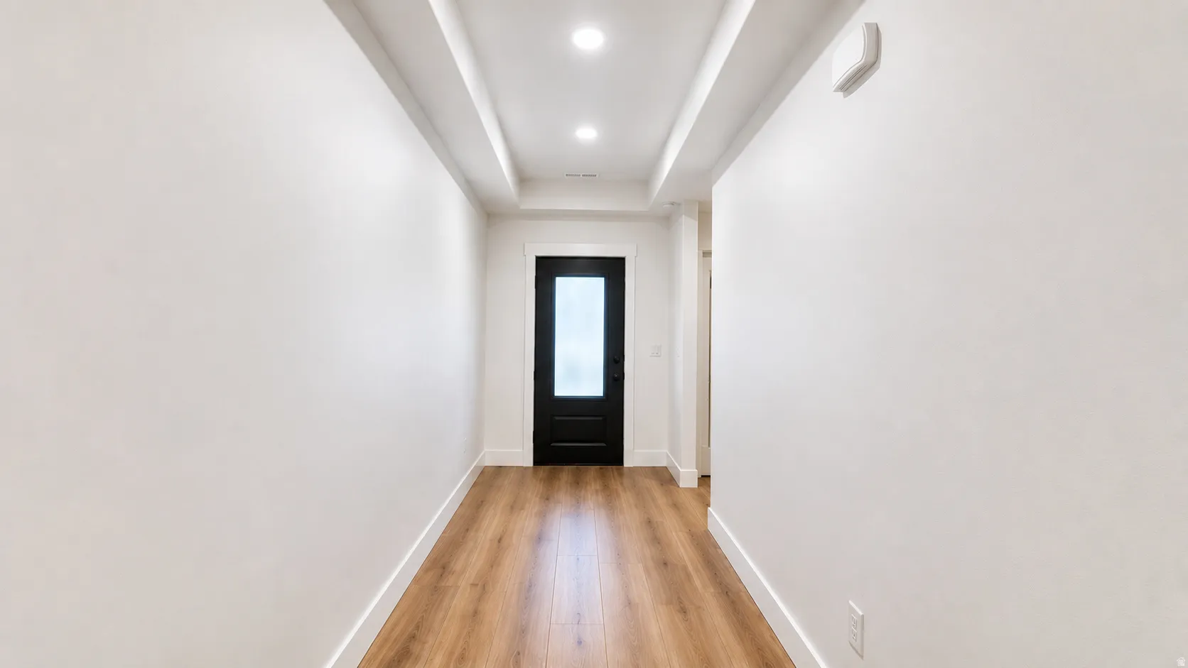 Recessed ceiling lighting, wood-finish flooring, white wall finishes, crown molding, and a black paneled door with frosted glass