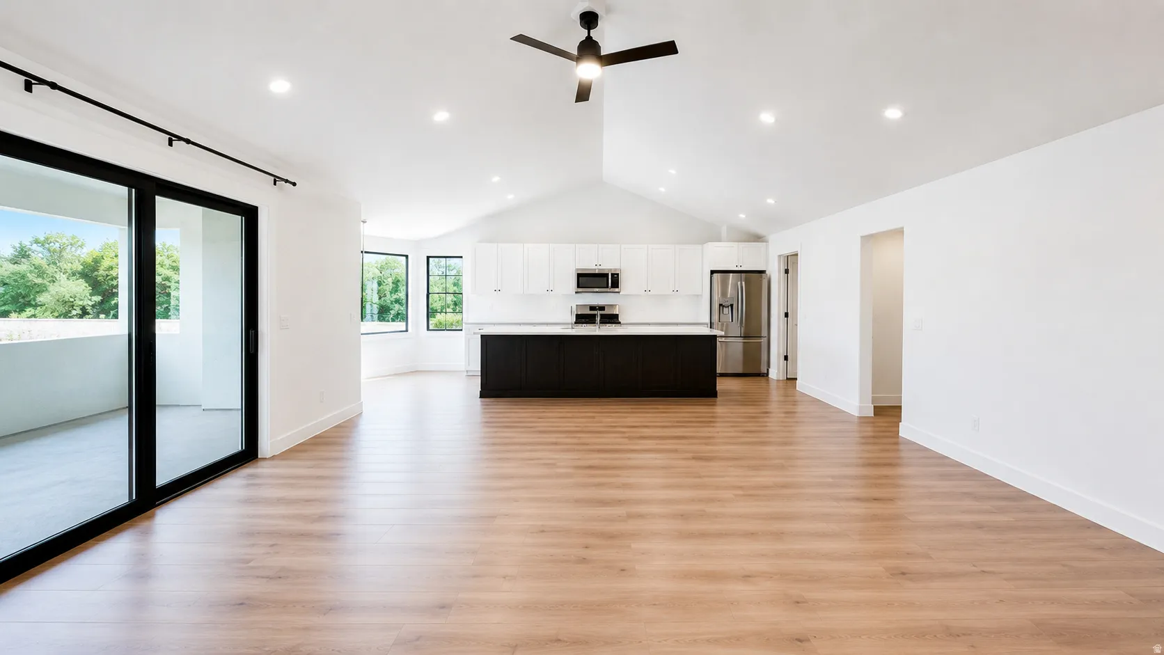 Vaulted ceilings, wood-finish flooring, recessed lighting, and a modern kitchen featuring an island with a contrasting base and stainless steel appliances
