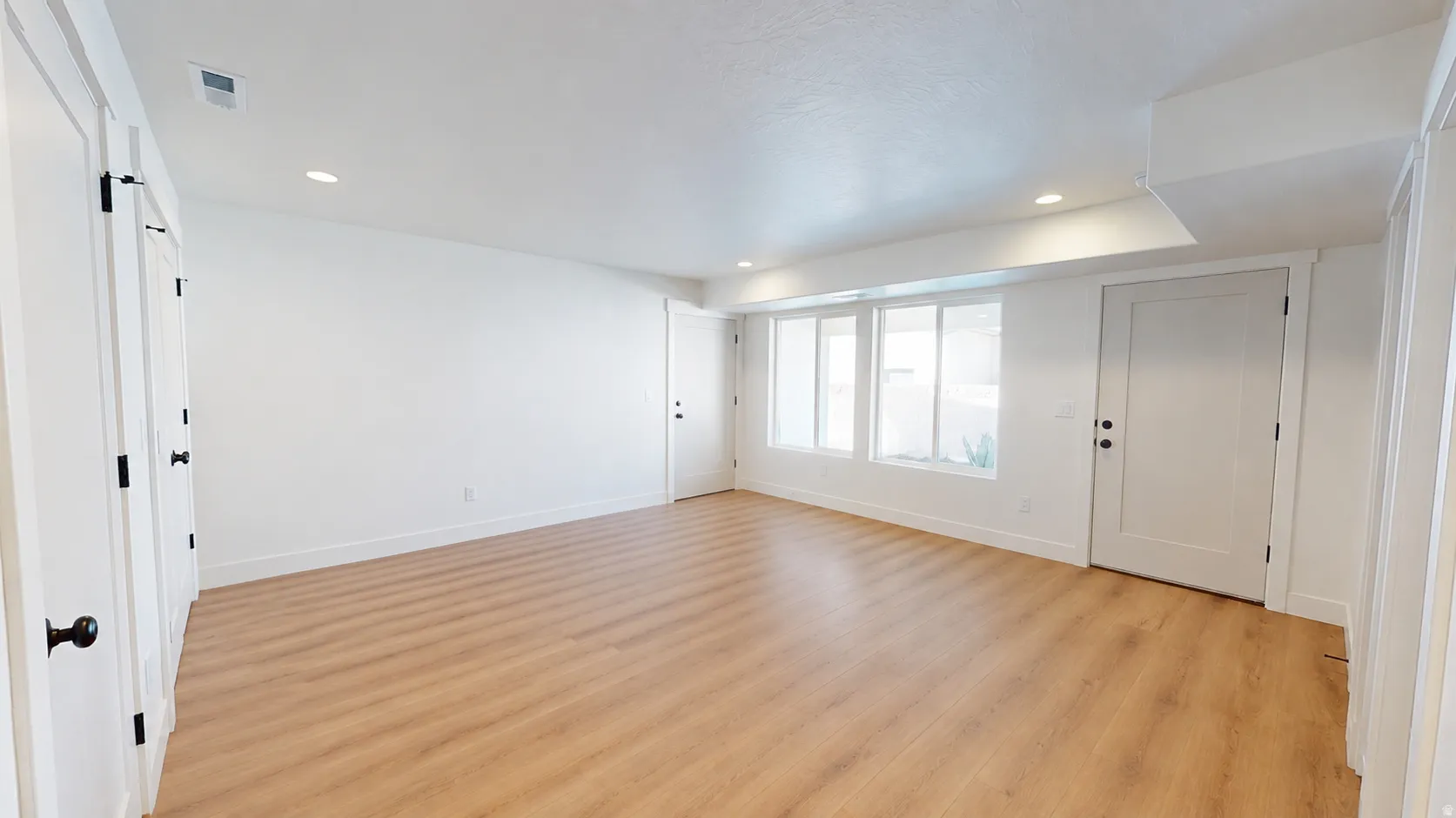 Recessed lighting, wood-finish flooring, multiple white paneled doors, and a series of windows