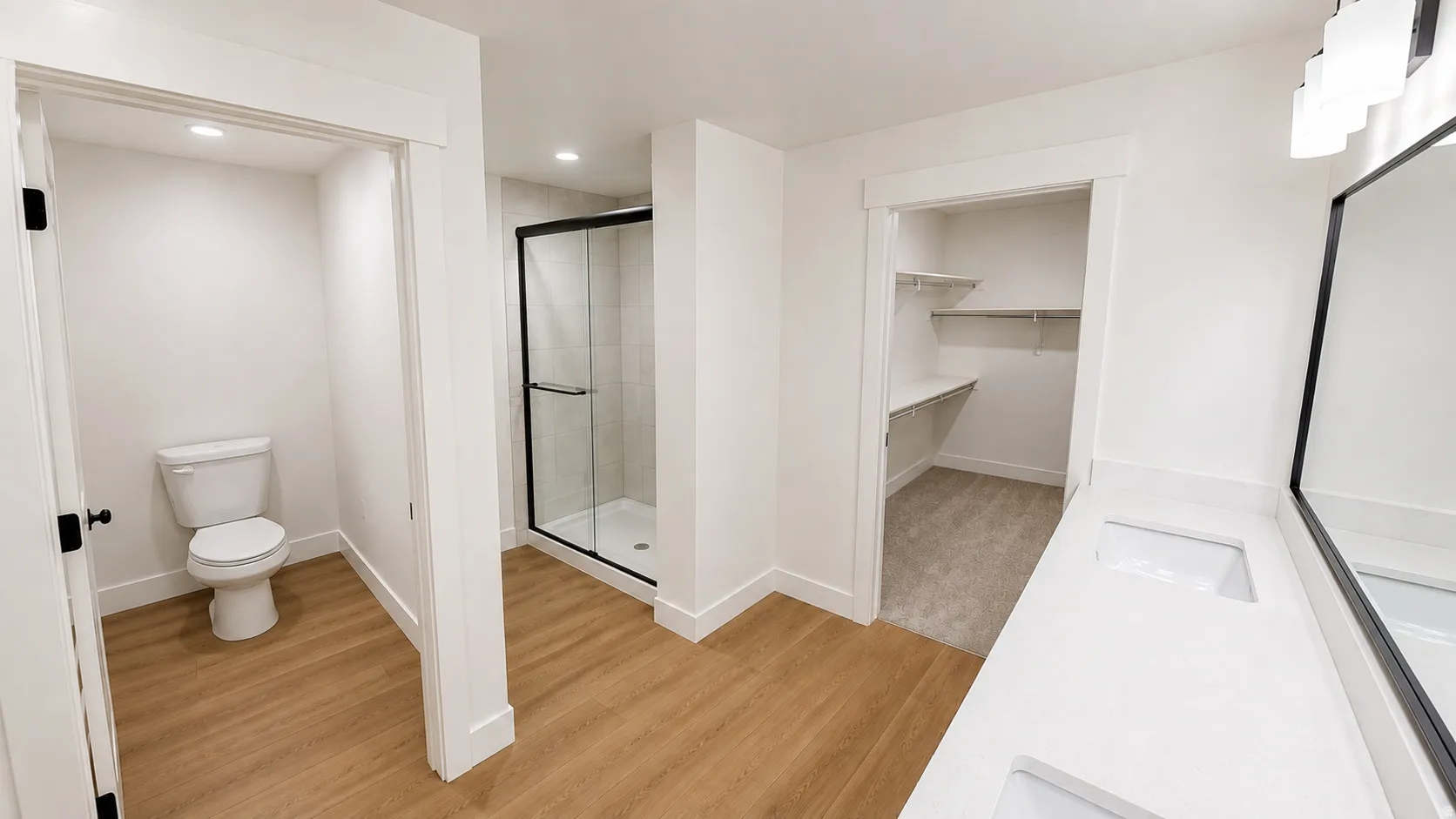 Dual vanity with undermount sinks, wood-finish flooring, black-framed shower enclosure, and a walk-in closet with built-in shelving