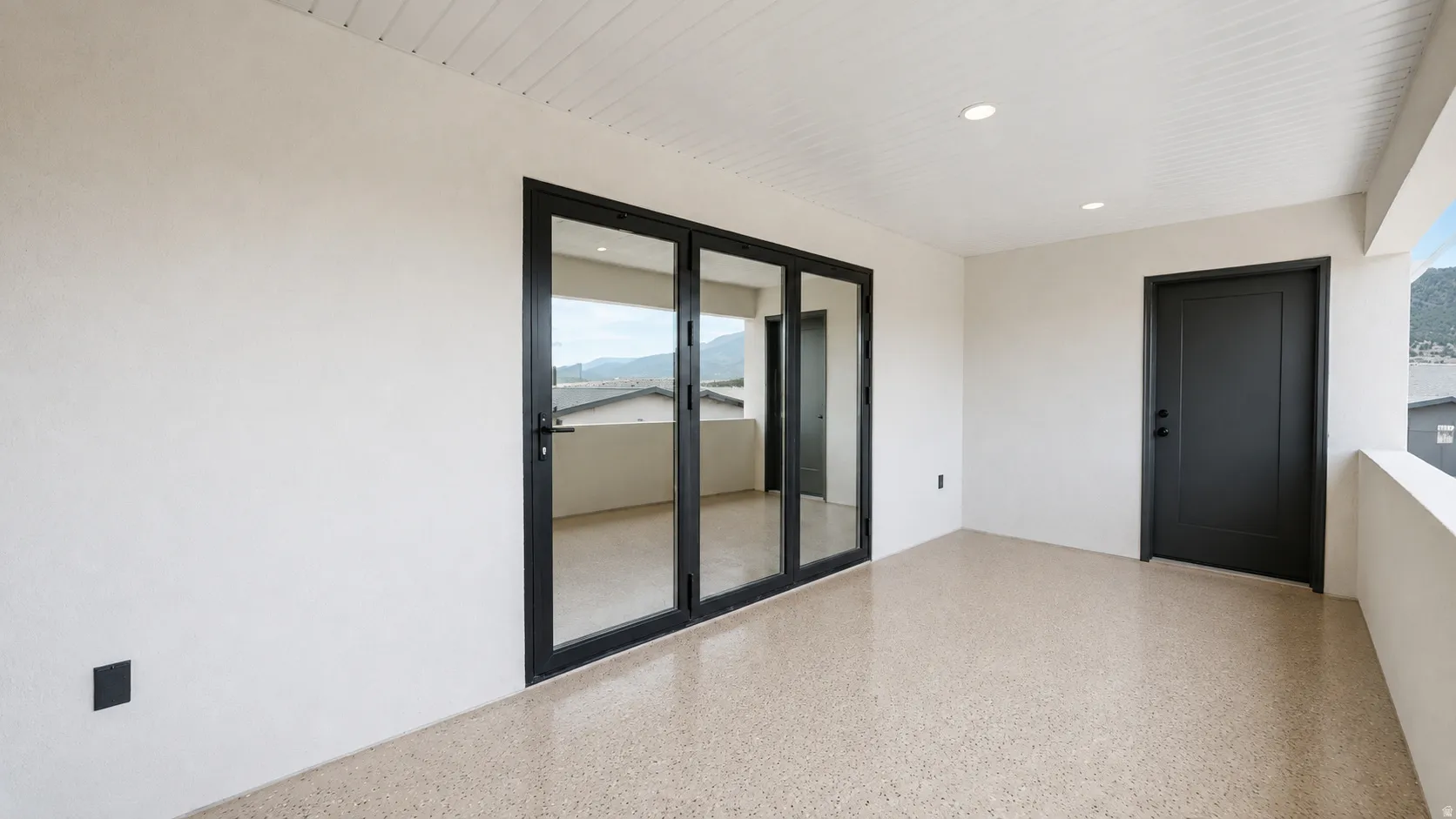 Spacious outdoor patio featuring durable aggregate flooring, recessed lighting, and a solid exterior door