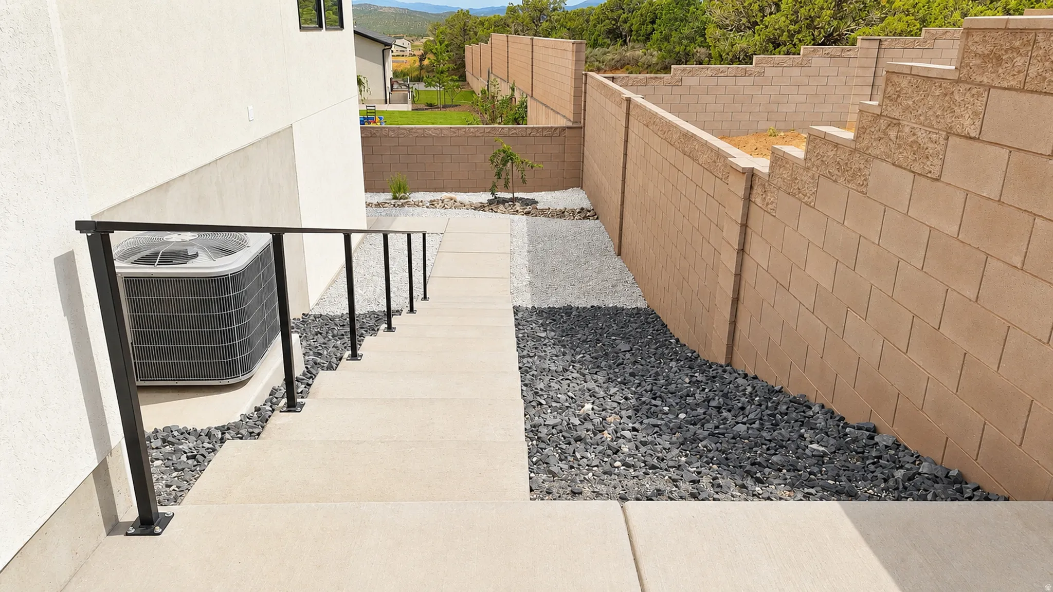 Concrete walkway with a black metal handrail, flanked by decorative dark and light gravel