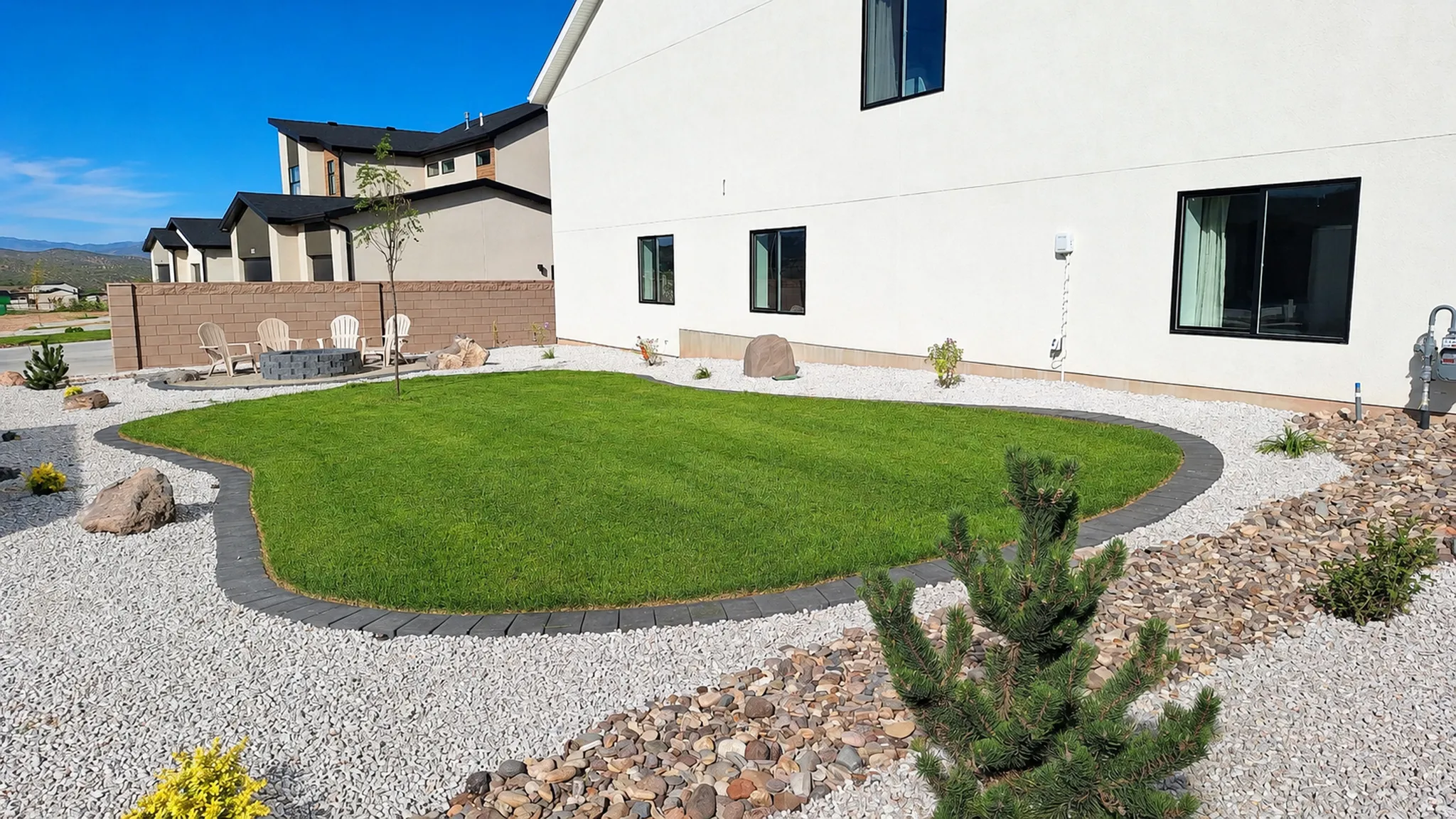 Manicured lawn with paver edging, surrounded by decorative white gravel and river rock landscaping