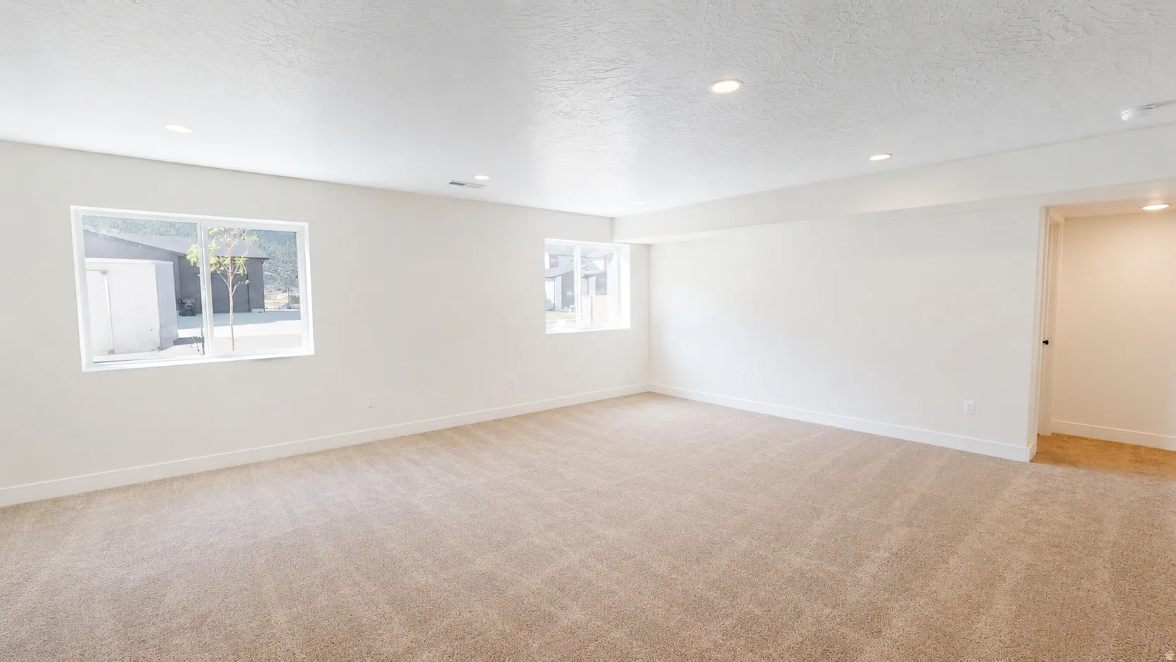 Spacious room featuring neutral carpeting, recessed lighting, and multiple windows