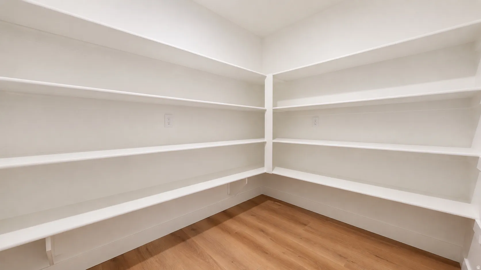 Spacious walk-in pantry with extensive built-in shelving, white walls, and wood-finish flooring