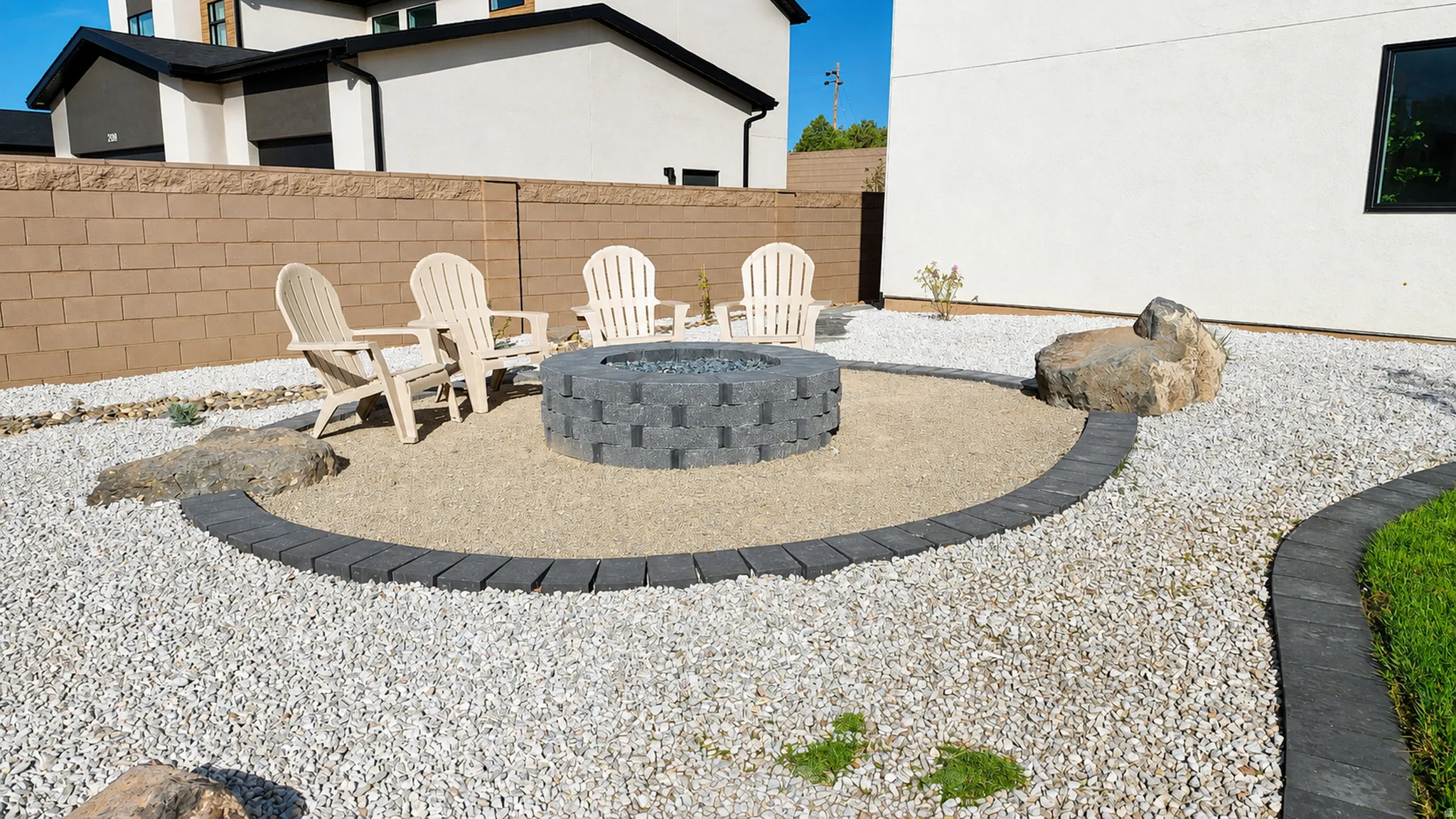 Landscaped backyard featuring a built-in fire pit, decorative rocks, and a gravel ground cover