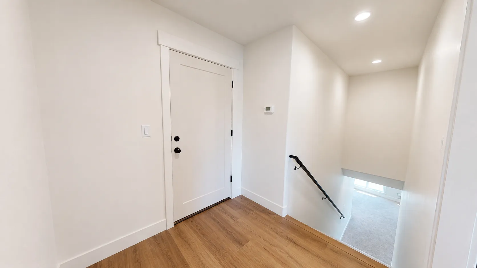 White painted door with black hardware, wood-finish flooring, recessed lighting, and a dark metal handrail