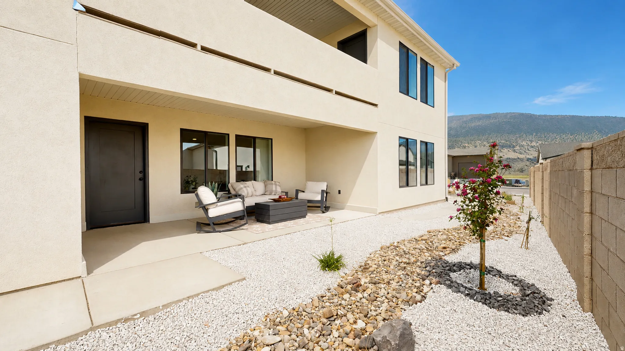 Rear patio with a concrete slab, upper-level balcony, xeriscape landscaping, and a privacy wall