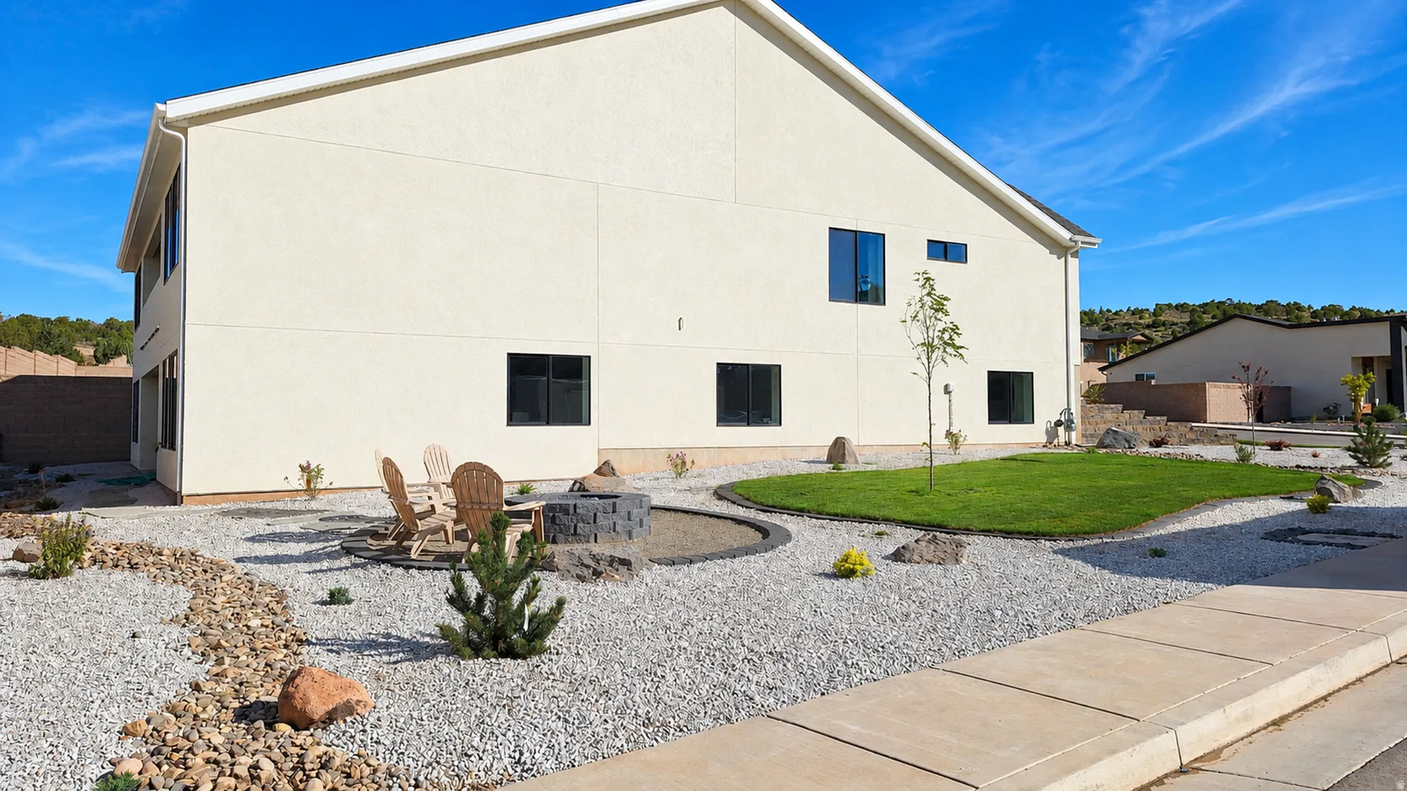 Expansive backyard featuring a fire pit, integrated seating area, manicured lawn, and decorative gravel landscaping