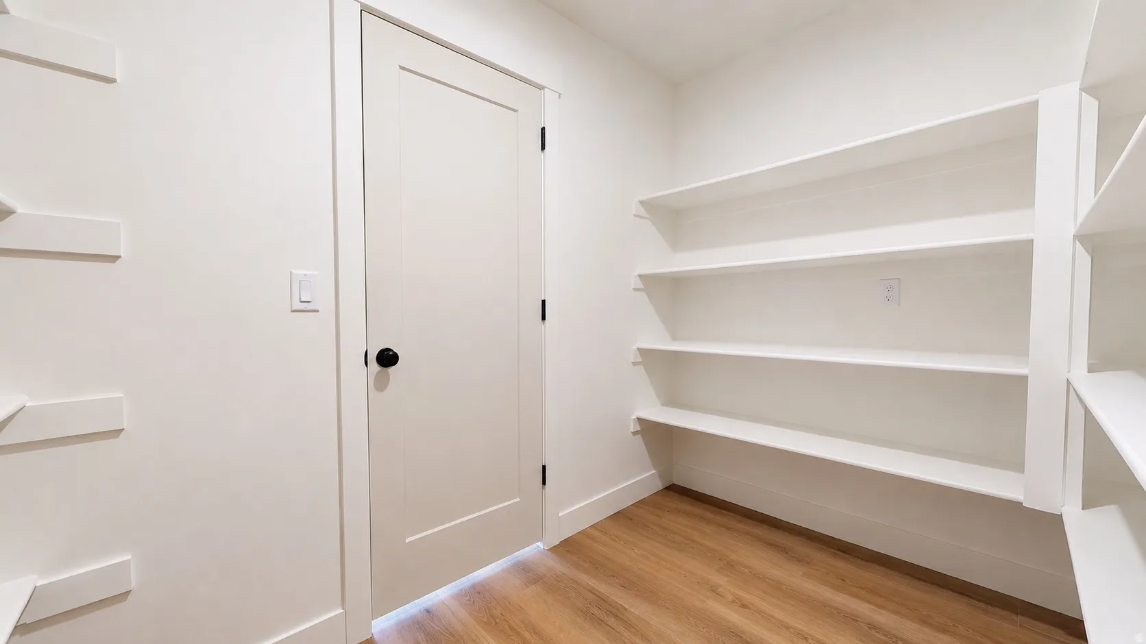 Walk-in pantry featuring extensive built-in shelving, a neutral color palette, wood-finish flooring, and a paneled interior door with a matte black knob